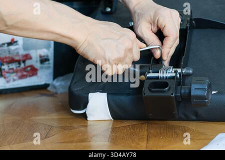 Hands adjusting spring mechanism with wrench on black chair base. Close-up of hands using adjustable wrench to tighten spring mechanism on black Stock Photo
