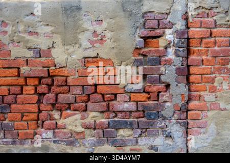 Old damaged red bricks and brickwork on a wall with crumbling and failing render coating. Plaster and render falling off of red brick wall. Stock Photo