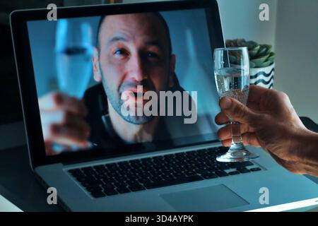 Young man drinking champagne holding sparkler talking to friends on virtual zoom video call celebrate happy new year party in distance online conferen Stock Photo