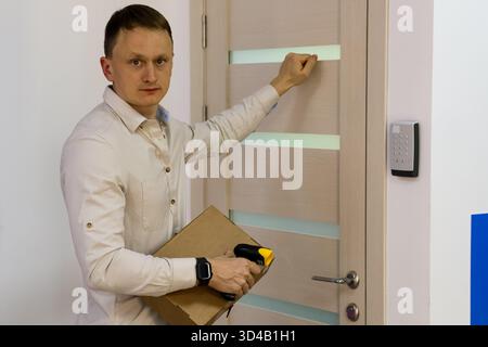 Man knocking on door holding package and scanner. Employee knocking at delivery point door with parcel and handheld scanner Stock Photo