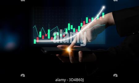 A hand interacts with a smartphone displaying stock market trends on the screen, illustrating data analysis and investment growth in a digital economy Stock Photo