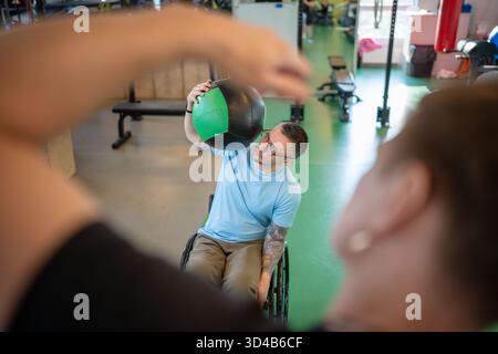 Man athlete in wheelchair doing upper body workout with heavy ball, building strength after injury. Stock Photo