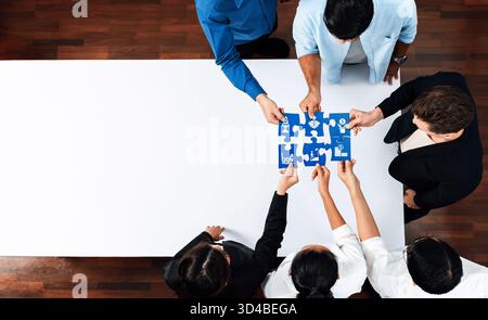 A diverse group of professionals engages in teamwork around a table, collaboratively solving a puzzle, which symbolizes innovation and effective Stock Photo