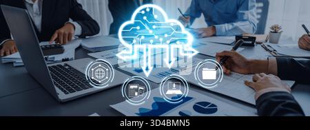 A diverse business team collaborates on cloud computing solutions using laptops and smart devices, surrounded by charts and documents in a modern Stock Photo