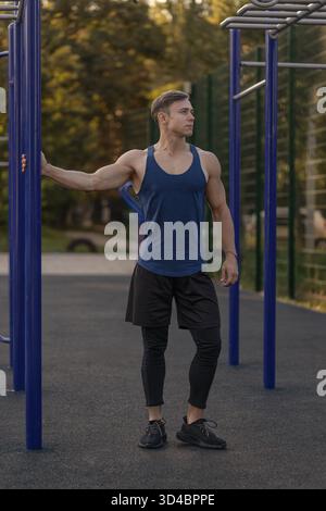 male athlete stands confidently on a sports ground wearing headphones. He is focused and ready for his workout showcasing dedication to fitness during the late afternoon light. Stock Photo
