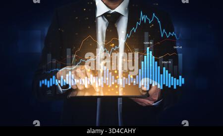 A businessman uses a tablet to analyze financial data, displaying stock market graphics and charts, representing trends and investment opportunities Stock Photo