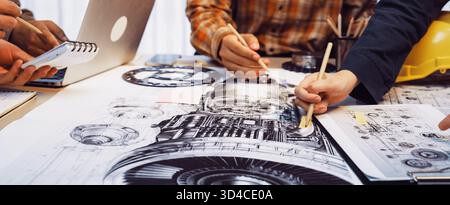 A collaborative workspace with hands working on engineering designs, featuring sketches, a laptop, tools, and technical drawings, showcasing Stock Photo