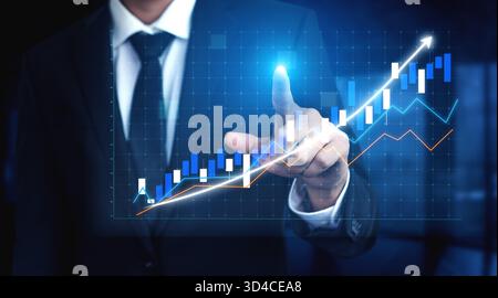 A confident businessman points at a digital graph displaying upward trends in financial performance, symbolizing growth, investment strategy, and Stock Photo