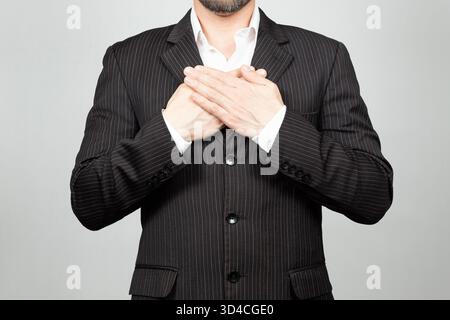 Close up to a businessman on suit doing a thankful expression with his hands over his chest and a white background Stock Photo