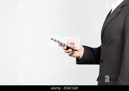 Close up to a businessman on suit at the right side of the screen holding a smart phone with his hand and a white background Stock Photo