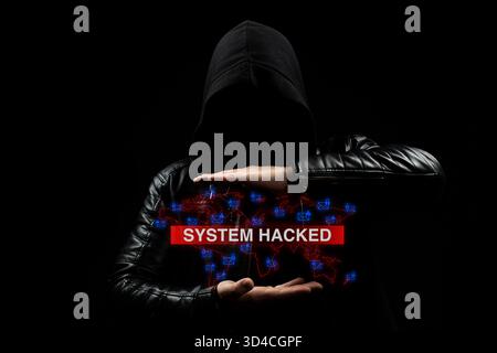 Close up to a faceless hooded hacker man in the shadows holding in middle of his hands a warning of system hacked with phishing concept Stock Photo