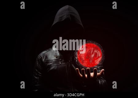 Close up to a faceless hooded hacker man in the shadows with a digital red earth globe in his left hand Stock Photo