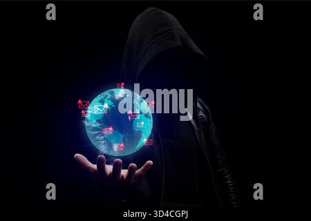 Close up to a faceless hooded hacker man in the shadows holding a globe earth with spam and phishing emails concept Stock Photo