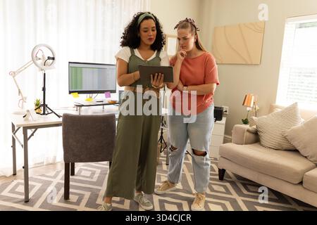 Diverse female colleagues reviewing spreadsheet on monitor in home office, with tablet, ring light Stock Photo