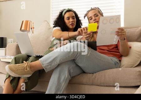 Diverse female friends collaborating on couch in living room, with printed charts and sticky note Stock Photo