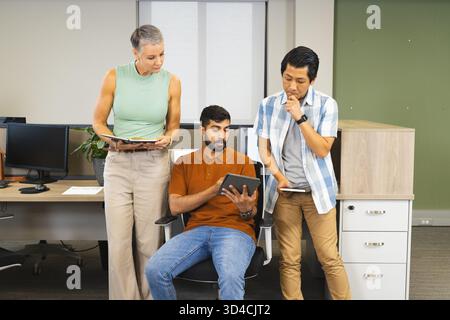 Collaborating Diverse coworkers reviewing tablet in modern open-plan office, with notebook Stock Photo