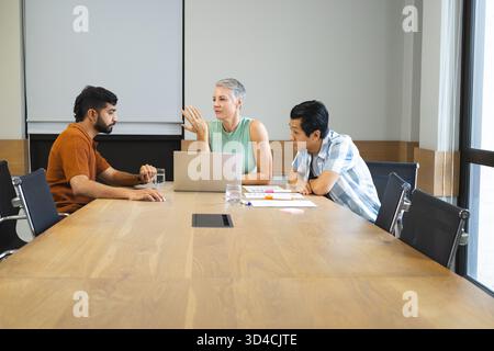 Diverse coworkers discussing project details in meeting room, with silver laptop and sticky notes Stock Photo