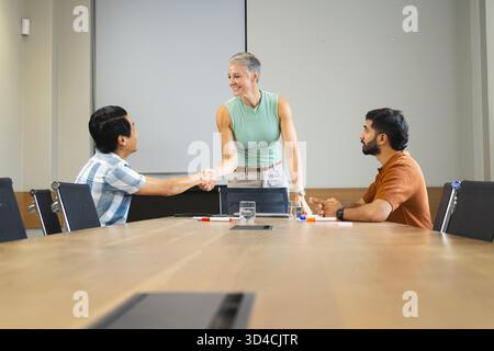 Greeting Diverse business associates shaking hands at meeting table in meeting room, with markers Stock Photo