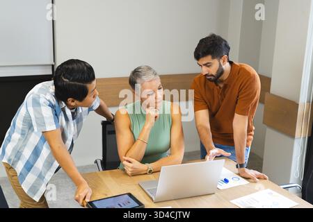 Collaborating Diverse coworkers reviewing data in meeting room, with laptop and printed charts Stock Photo