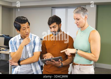 Collaborating instructor with students navigating tablet in computer lab, with desktop computers Stock Photo