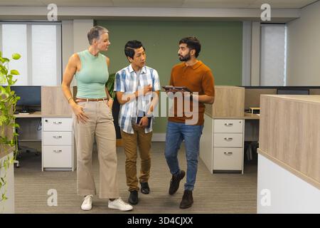 Walking diverse coworkers discussing work in modern open-plan office, with tablet and notebook Stock Photo