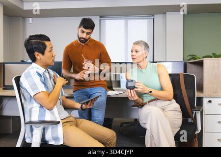 Diverse coworkers discussing project ideas in open office, with tablet, coffee mug and iced coffee Stock Photo