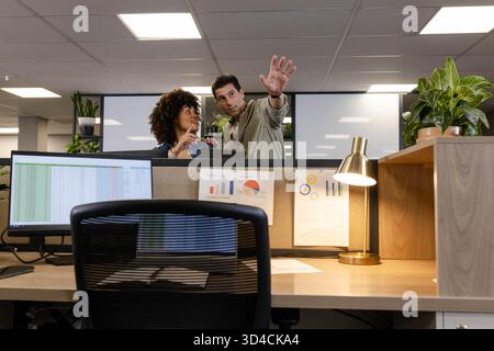 Diverse coworkers discussing spreadsheet data on monitor behind cubicle wall at office, with plants Stock Photo