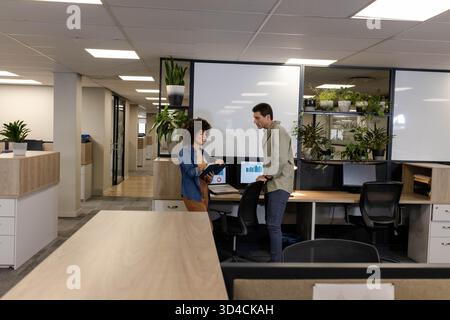 Discussing project goals diverse coworkers meeting in open-plan office, with tablet and whiteboard Stock Photo