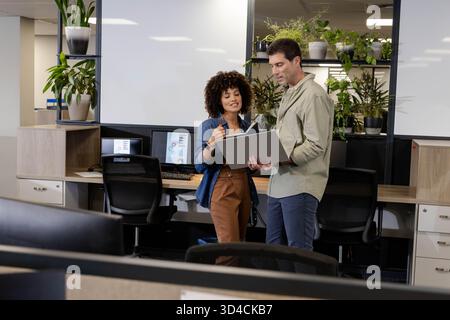 Diverse coworkers collaborating on brainstorming ideas in open office, with laptop and whiteboards Stock Photo