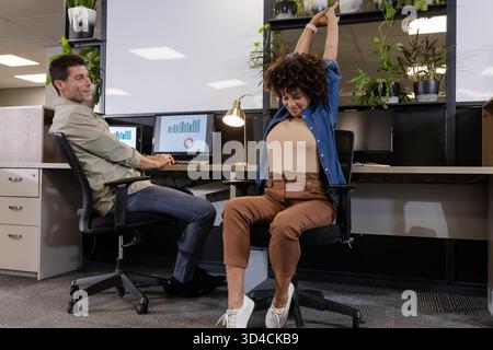 Working Diverse coworkers typing on dual monitors and stretching at desk in office, with plants Stock Photo