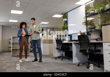 Discussing work Diverse co-workers standing in office, with tablet smartphone monitors, copy space Stock Photo
