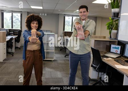 Diverse coworkers stretching arms in open-plan office, with laptop showing bar chart Stock Photo