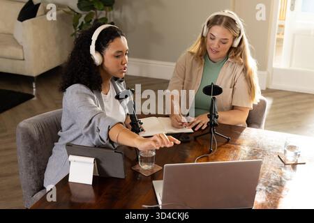 Recording podcast Diverse female colleagues collaborating at home office, with mics and laptop Stock Photo