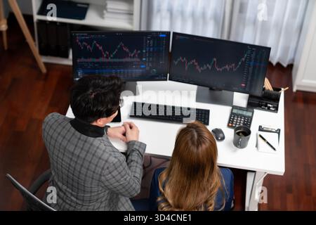 Top image view of analyzing successful Asian businesswoman looking at dynamic stock exchange data screen with businessman partner pointing value rate Stock Photo