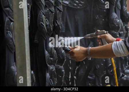 Focused worker painting fantasy costume with spray gun in workshop. close up of hands coating black armor prop, showing industrial process of creating Stock Photo