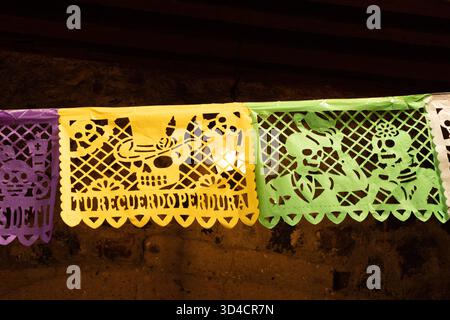 A colorful banner with a skull and a hat on it. The banner is in Spanish. Mexican Day of the Dead tradition, offerings, food, colors, decorations, and Stock Photo
