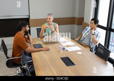 Analyzing charts Diverse coworkers collaborating at wooden table in office, with laptop and tablet Stock Photo