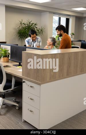 Collaborating Diverse coworkers sharing ideas at open-plan office desk, with dual monitors Stock Photo