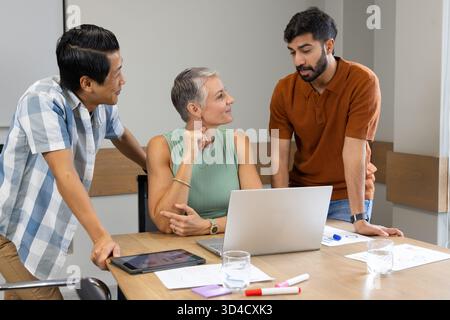 Collaborating Diverse coworkers analyzing charts around conference table in office, with laptop Stock Photo