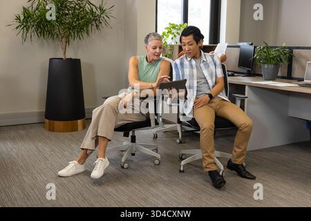 Collaborating Diverse coworkers studying tablet data in open-plan office, with stack of papers Stock Photo