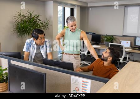 Chatting Diverse coworkers collaborating at workstations, with printed chart and computer monitors Stock Photo