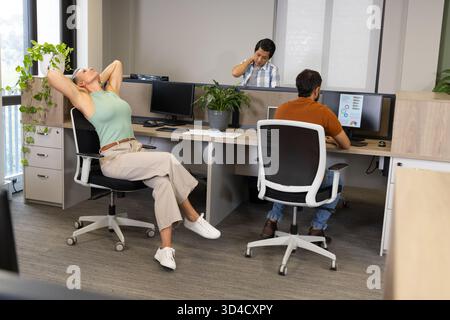 Diverse coworkers working and stretching in open-plan office, with computer monitors, copy space Stock Photo