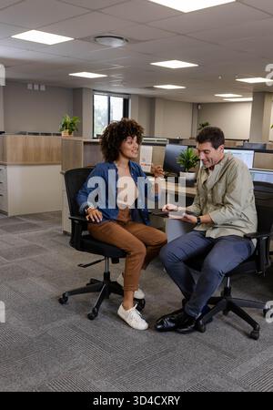 Diverse coworkers discussing project ideas in modern open-plan office, with tablet and monitors Stock Photo