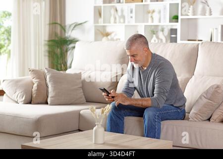 Happy senior man using cell phone sitting on a couch at home Stock Photo