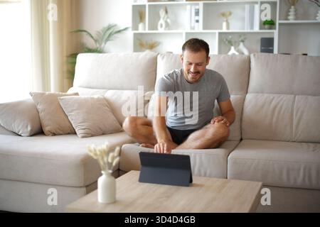 Man preparing online yoga class on tablet in a house interior sitting on a couch at home Stock Photo