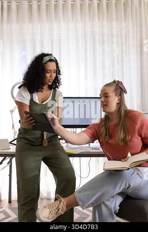 Collaborating diverse female colleagues reviewing spreadsheet in home office, with tablet, notebook Stock Photo