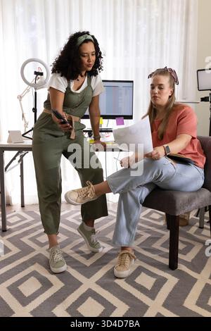 Collaborating Diverse female colleagues reviewing documents at desk in home studio, with ring light Stock Photo