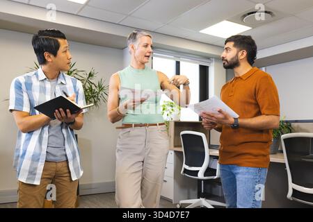Diverse coworkers collaborating in open-plan office, using printed charts and notebooks Stock Photo