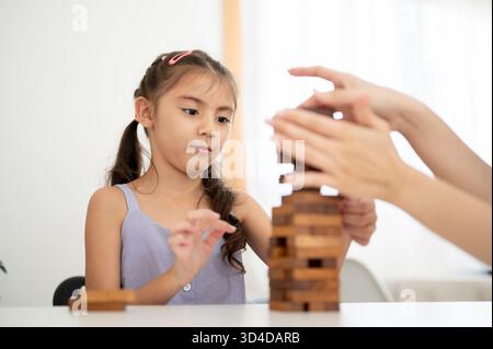Asian kid or a girl in purple shirt looking at her parent hand while playing a wooden tower building game together. Kids toys, Wooden blocks. Stock Photo