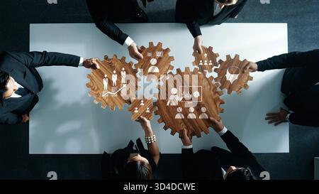 A high-angle view of a business team working together with wooden gears representing teamwork and strategy in an office space, emphasizing Stock Photo